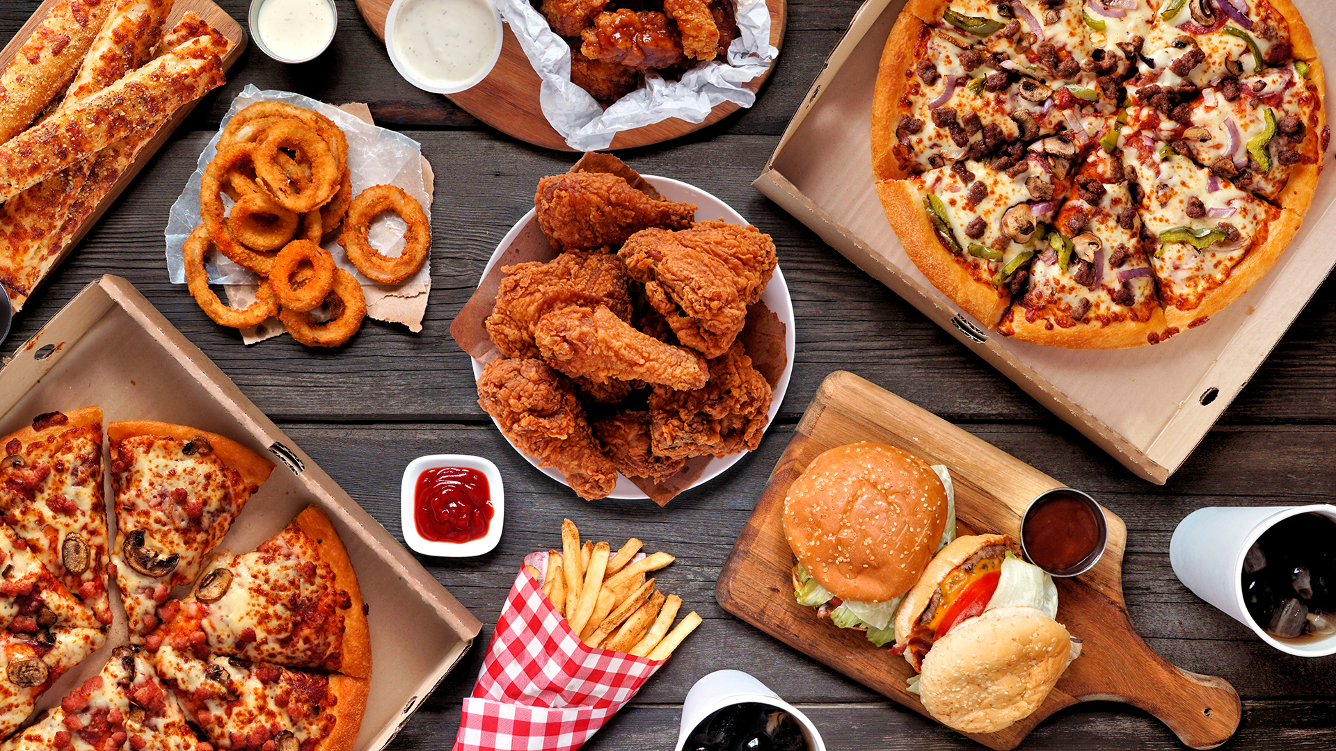 fried, processed and unhealthy foods like onion rings, fried chicken and soda are shown on a table