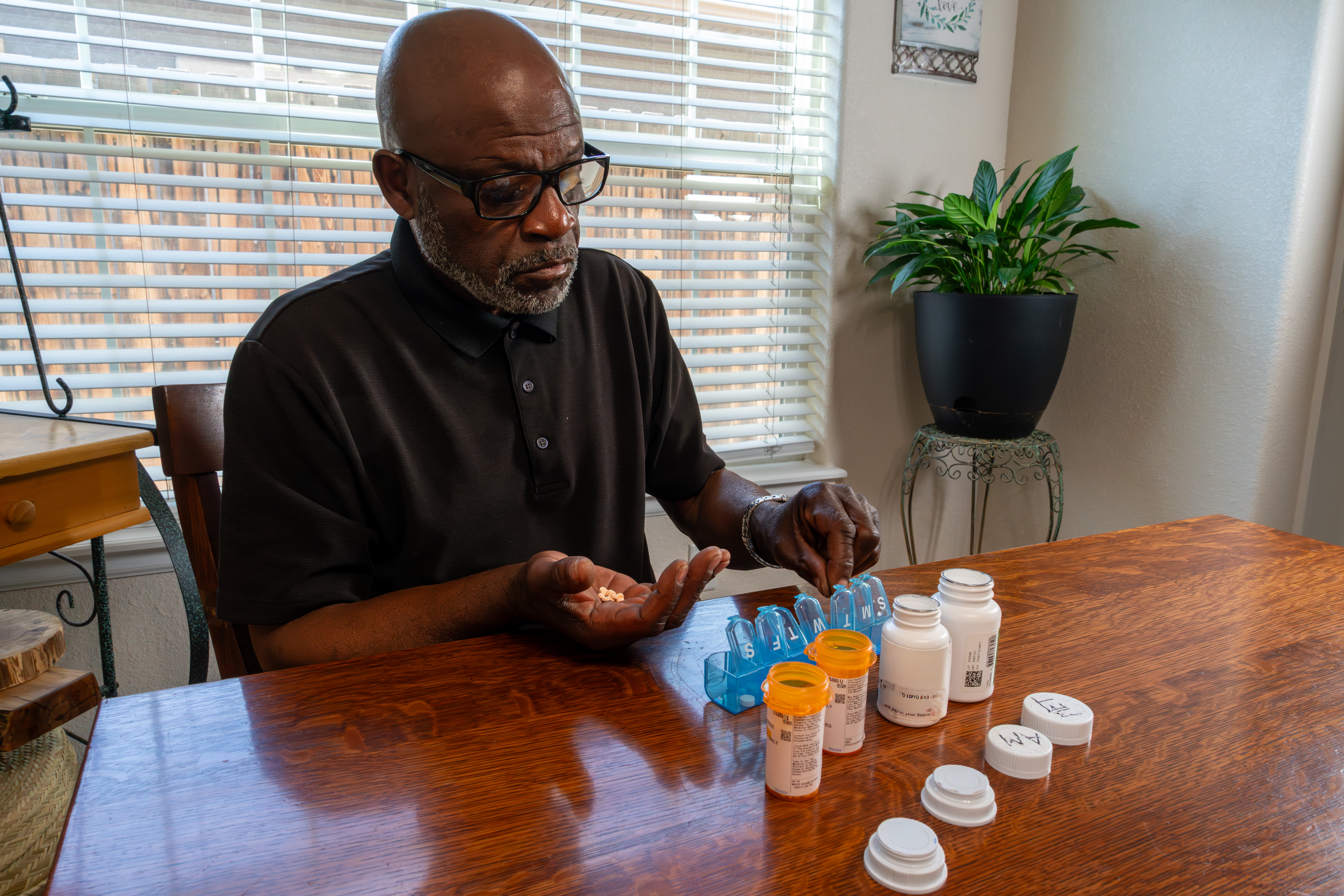 a man is shown sitting at a table and sorting his medications into a pill planner