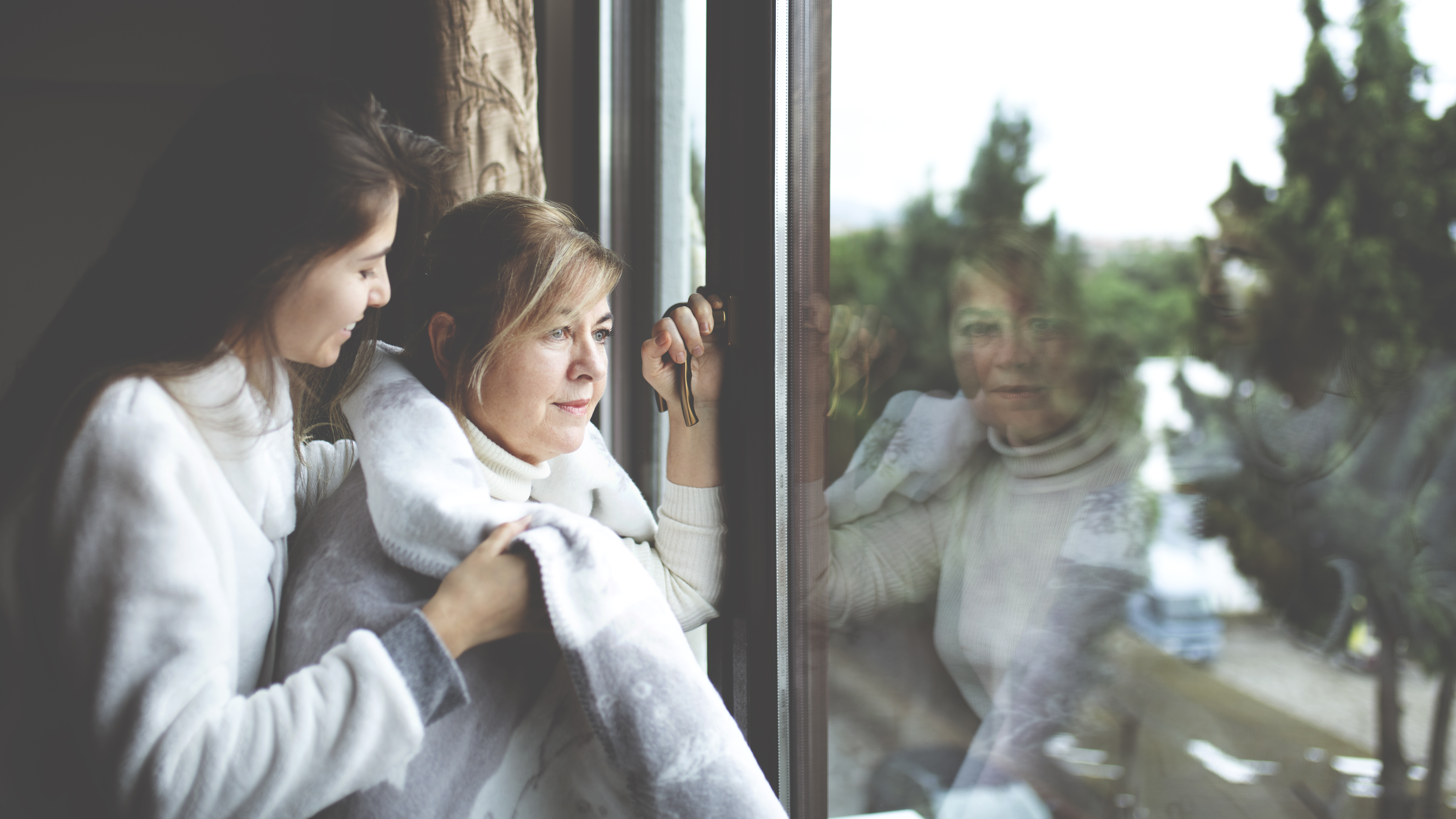 woman looks out a window while her reflection stares back at her