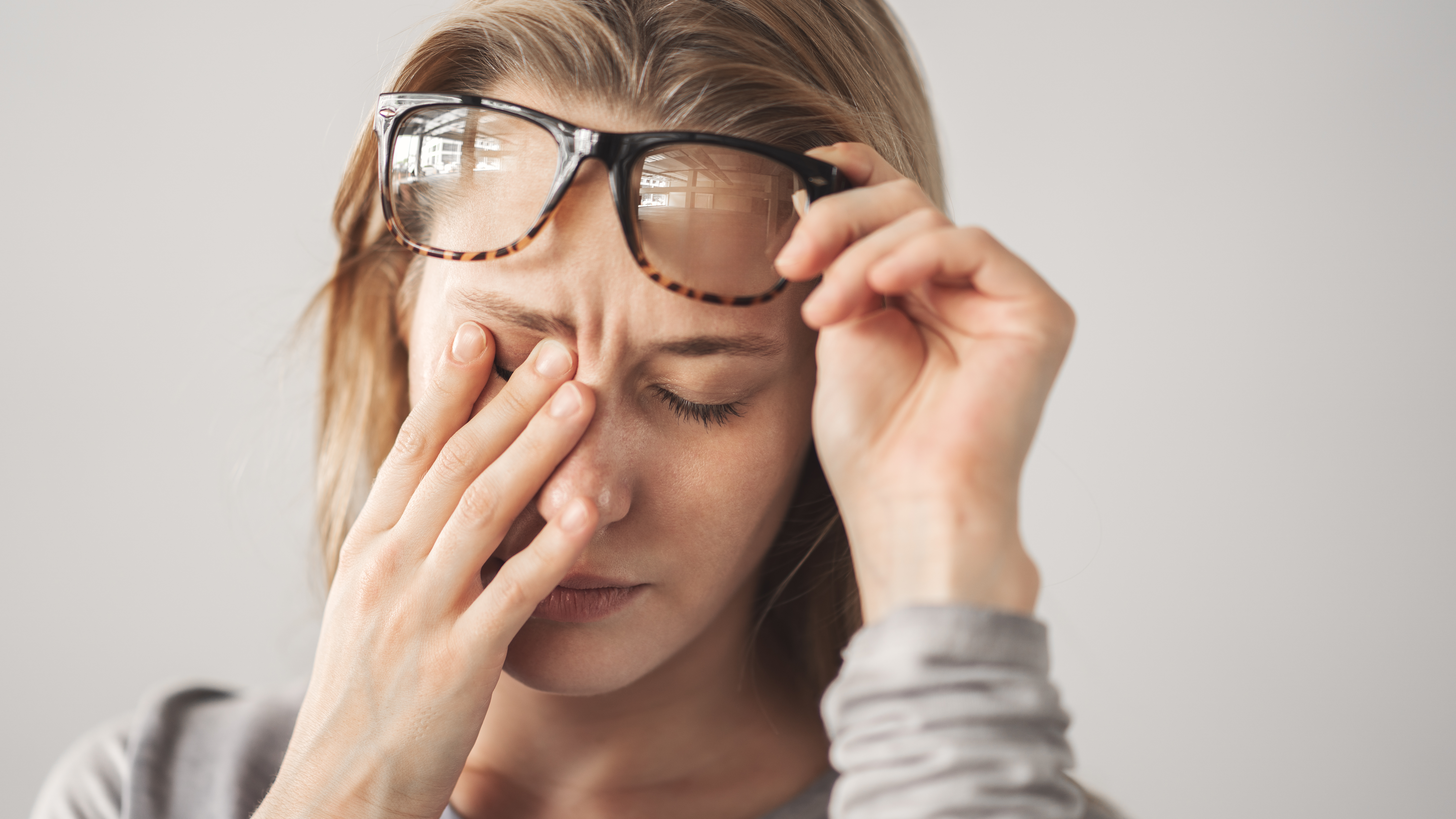 a woman pushes her glasses to the side while massaging her eyes and forehead from pain