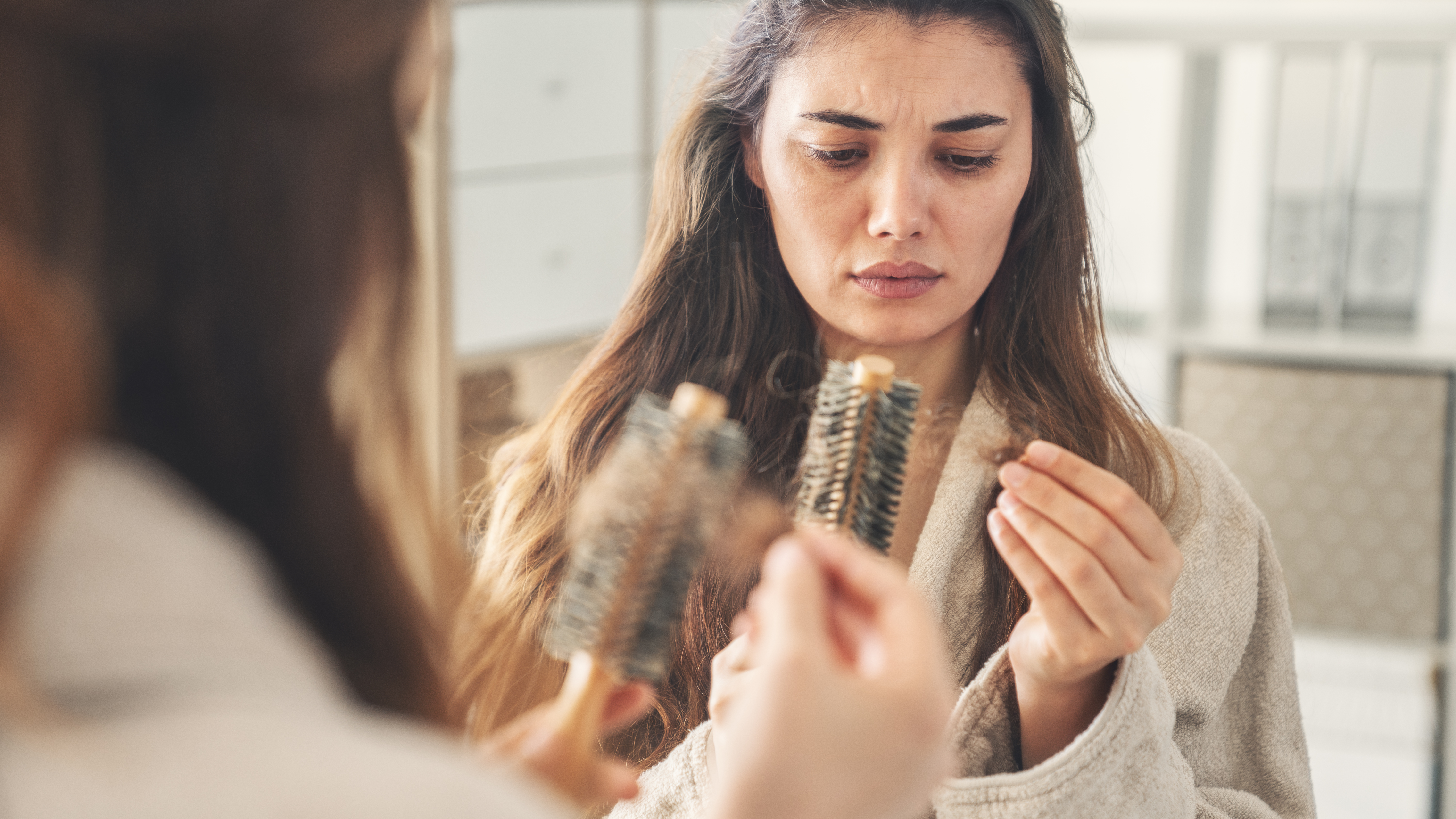a woman looks with concern at her comb filled with clumps of hair